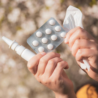 Two hands holding nasal spray, pills and a handkerchief