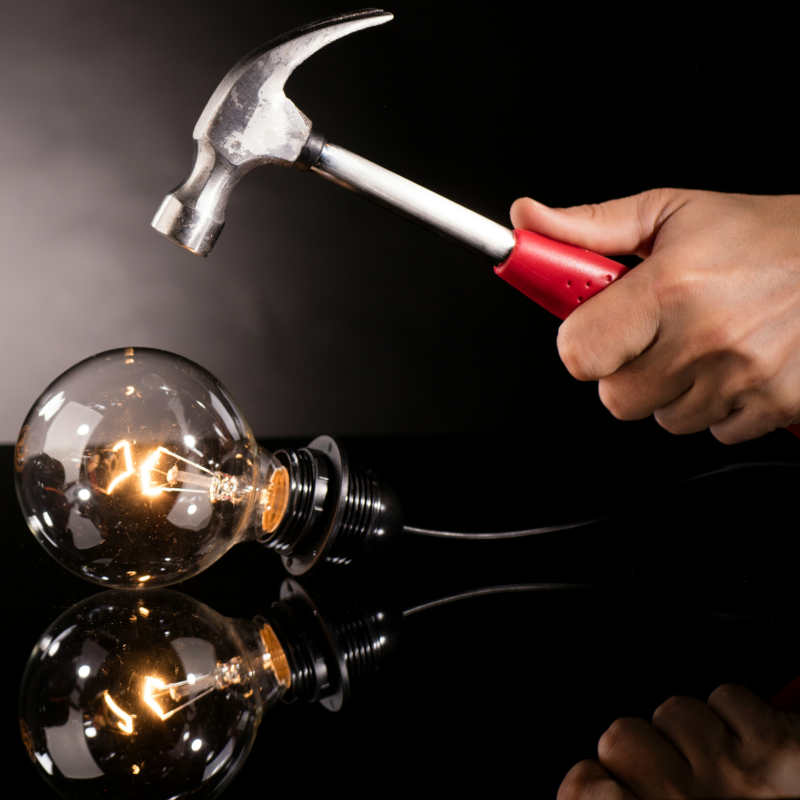 A hammer that looks like it's about to smash a light bulb, with a camera beside it
